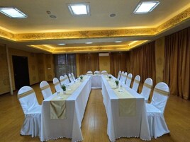 Un salón de conferencias con una larga mesa, sillas blancas y un candelabro.