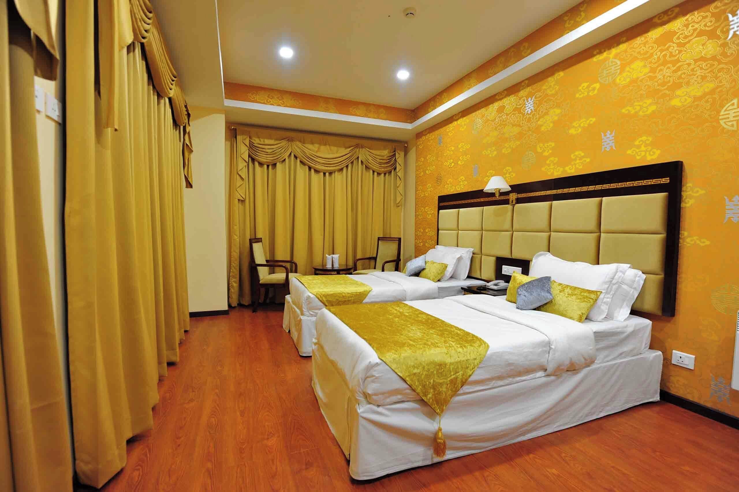 Habitación de hotel con dos camas, un ventanal con cortinas, suelo de madera y un cabecero decorativo.