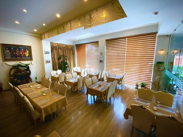 A dining area with multiple tables and chairs, large windows with blinds, and a decorative ceiling. - 33 Soksoom Centre For Well-Being & Happinesss (Thimphu)