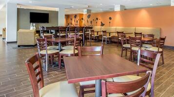 A restaurant with multiple tables and chairs, a flat-screen TV mounted on the wall, and a patterned wall decoration.
