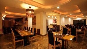 A restaurant with a long communal table and individual tables, warm lighting, and a modern ceiling design.