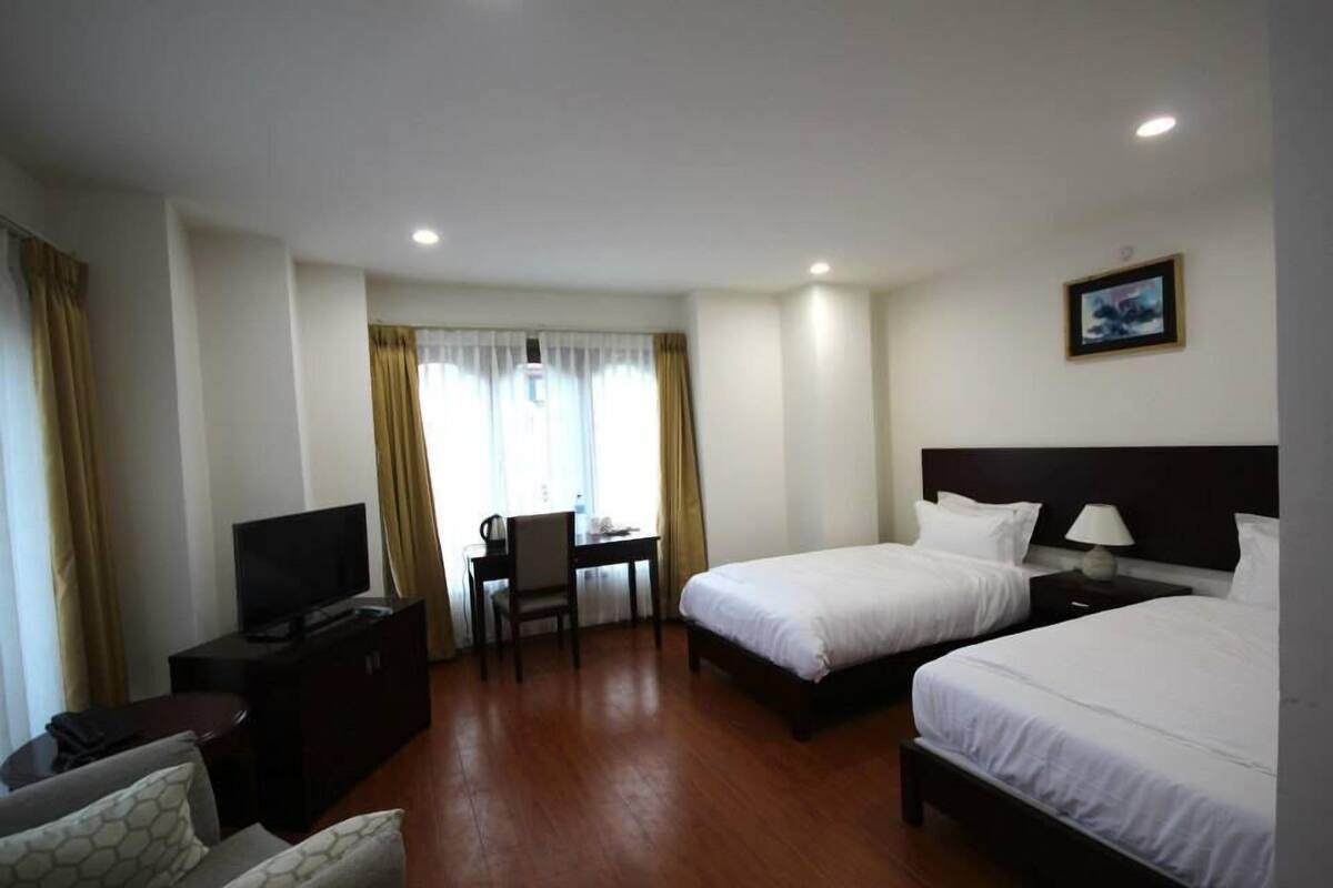 Habitación de hotel con dos camas, un escritorio con silla, televisor y un cuadro en la pared.