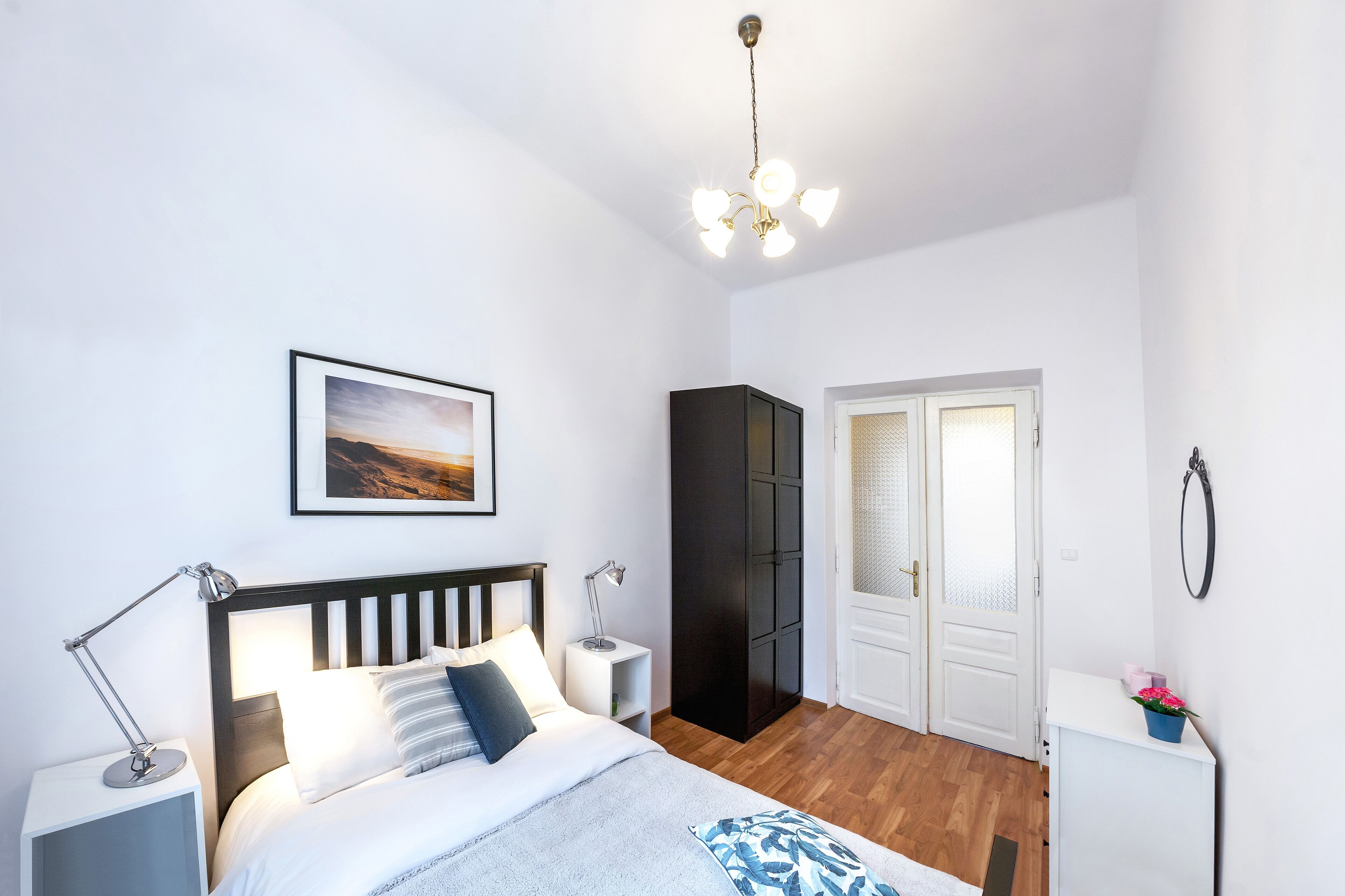Une chambre à coucher avec un lit, des lampes de chevet, une armoire, une porte et une petite table sur laquelle est posée une plante.
