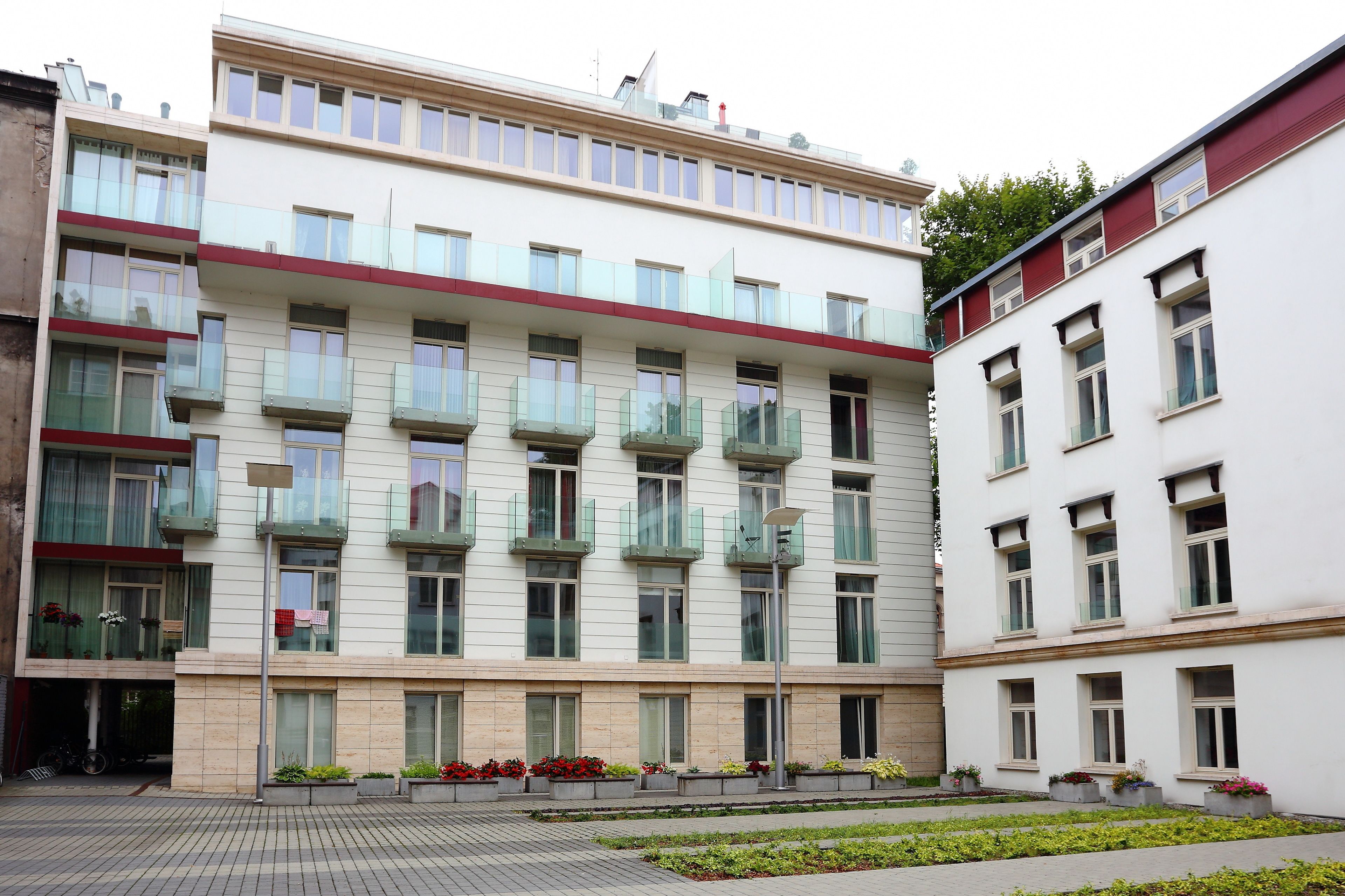 A multi-story building with balconies, large windows, and a paved courtyard with flower beds.