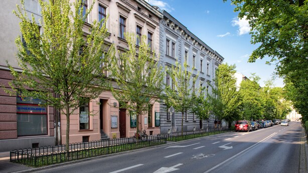 A street lined with trees and a row of buildings with a clear road and directional arrows. - FriendHouse Apartments – Old City (Kraków)