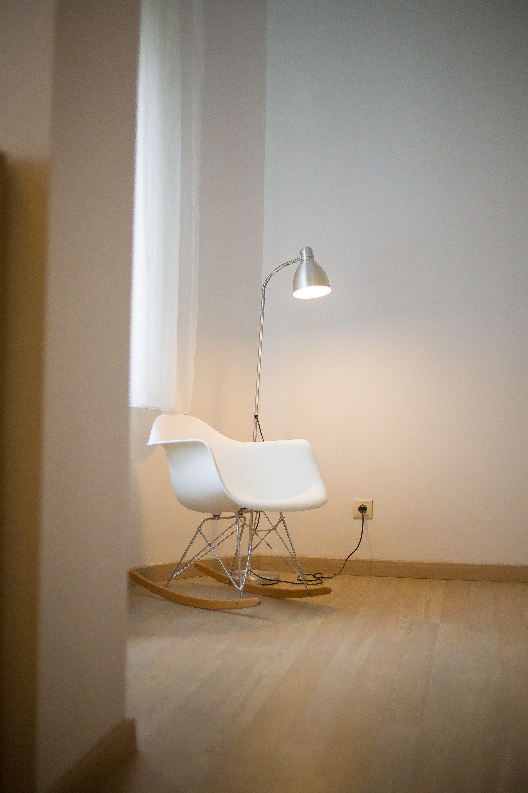 Une chambre moderne avec un fauteuil à bascule blanc, une lampe sur pied et un plancher en bois.
