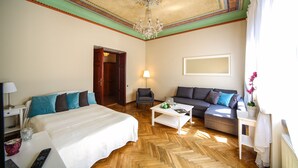 A hotel room with a large bed, a sofa, a coffee table, a desk with a lamp, and a chandelier. - FriendHouse Apartments – Old City (Kraków)