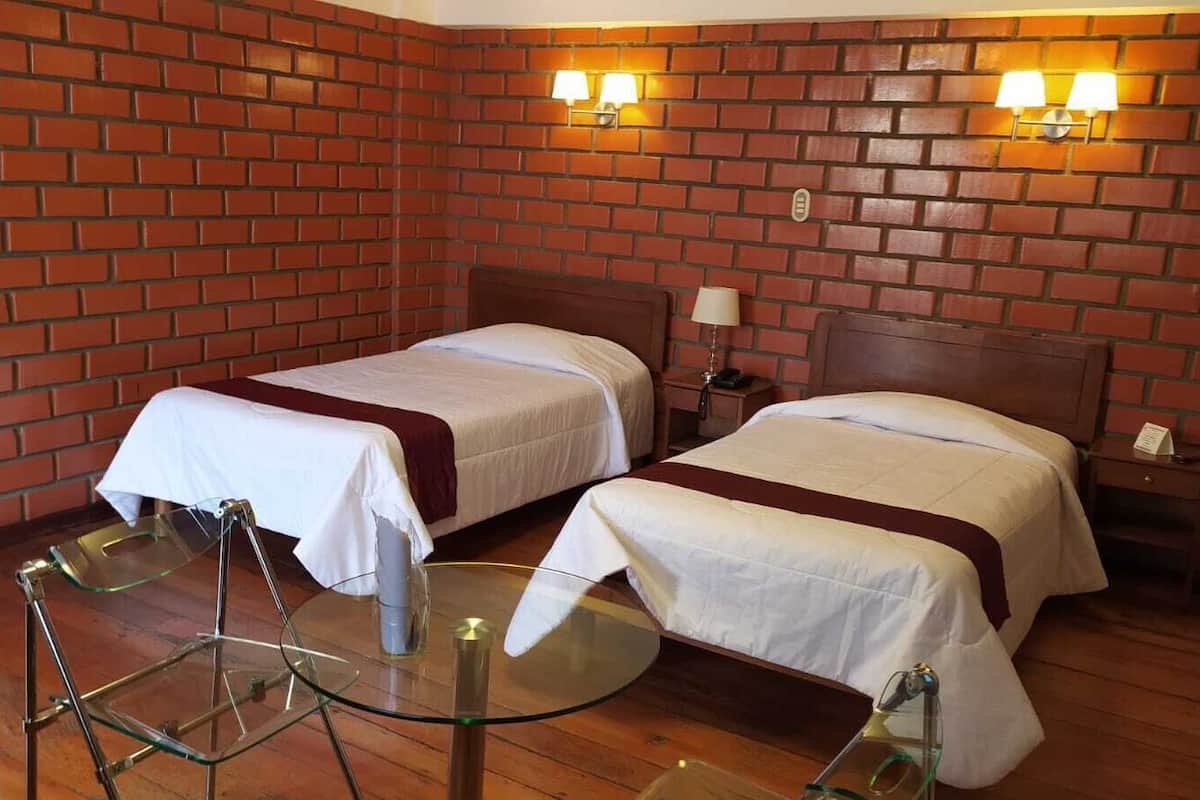 Una habitación de hotel con dos camas, una mesa de vidrio y paredes de ladrillo.