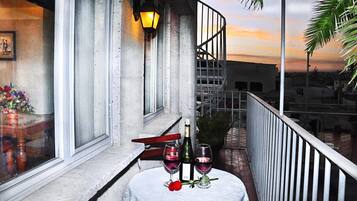 A balcony with a table set for two, featuring a bottle of wine and two glasses, a red rose, and a candle.