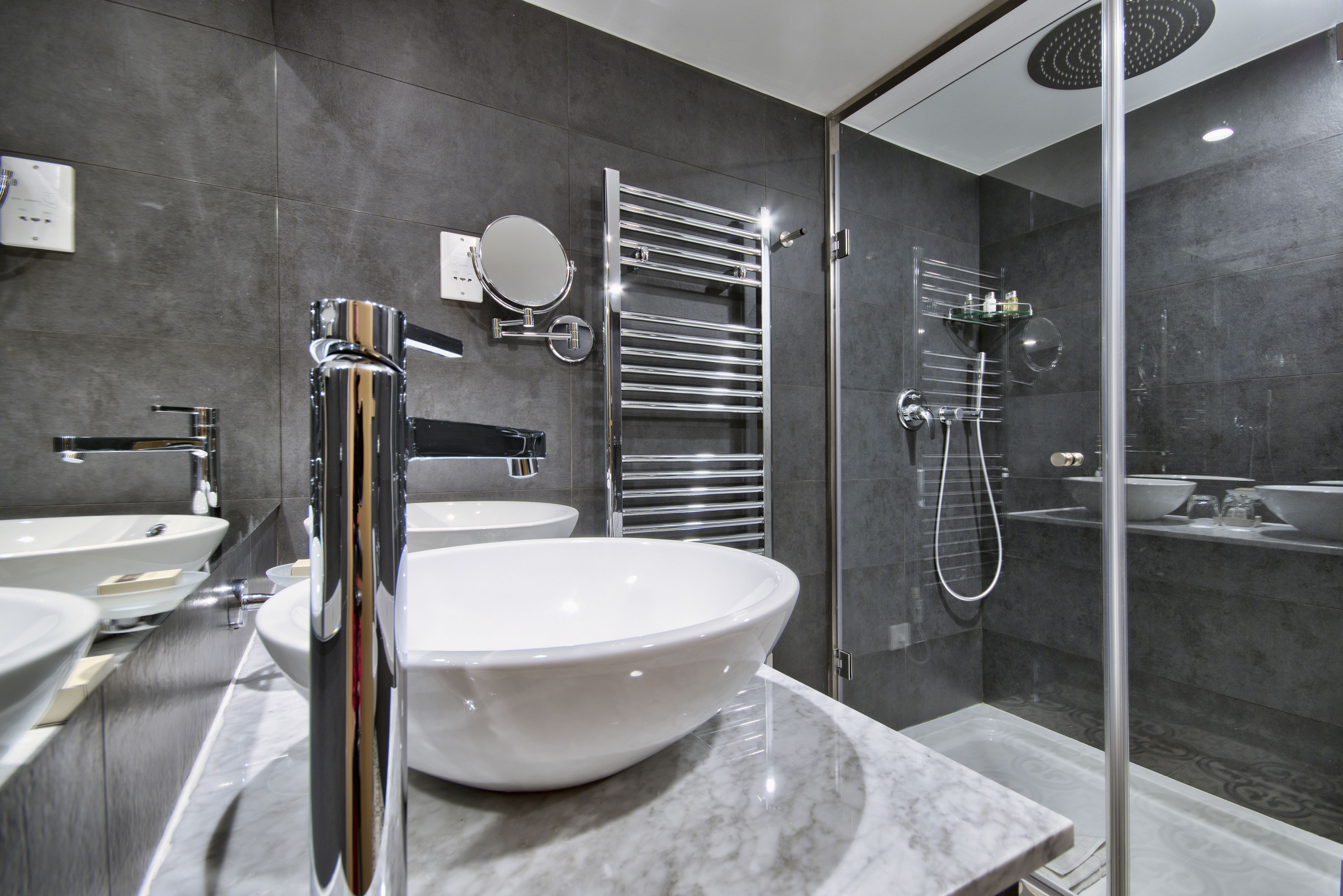 A modern bathroom with a large white sink, a glass-enclosed shower, and a chrome towel rack.