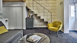 Una sala de estar moderna con una mesa de centro de vidrio, un sofá, un sillón amarillo y una escalera frente a una pared de ladrillo.
