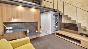 Una sala de estar moderna con un sofá, un televisor de pantalla plana, un escritorio con una lámpara y una escalera.