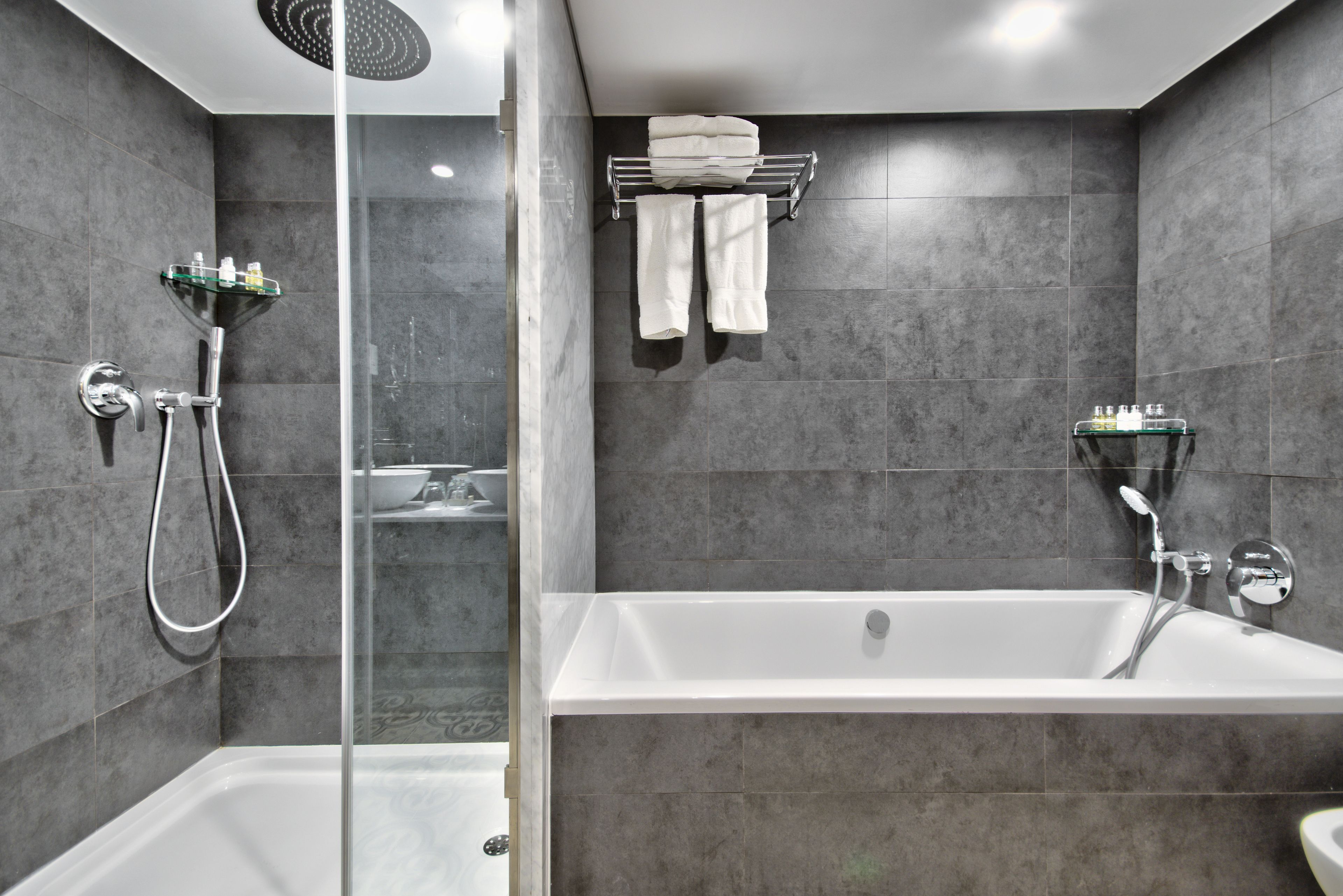 A modern bathroom with a glass-enclosed shower, a freestanding bathtub, and a towel rack with folded towels.