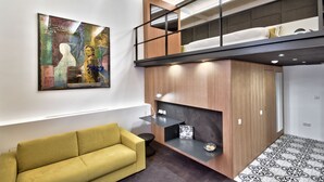 Un dormitorio tipo loft moderno con una cama litera, un sofá amarillo, una chimenea y un cuadro abstracto grande en la pared.