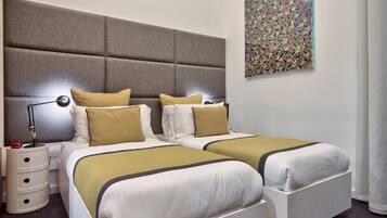 Une chambre d’hôtel avec deux lits, une grande tête de lit rembourrée, une lampe de chevet, une table de chevet et un tableau abstrait aux couleurs vives accroché au mur.