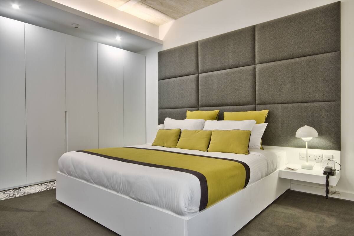 Un dormitorio moderno con una cama grande, un cabecero acolchado gris y una mesita de noche con una lámpara.