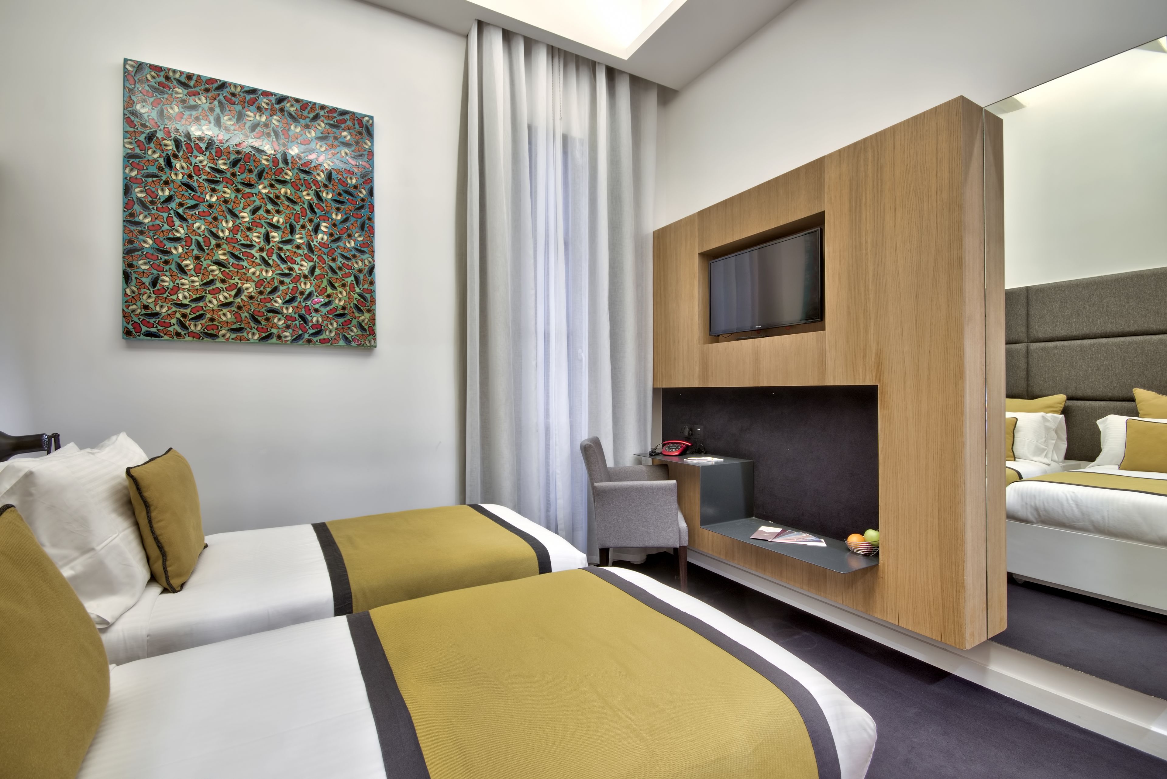 Habitación de hotel con dos camas, un escritorio con televisor, un cuadro abstracto grande y vistas a la ciudad.