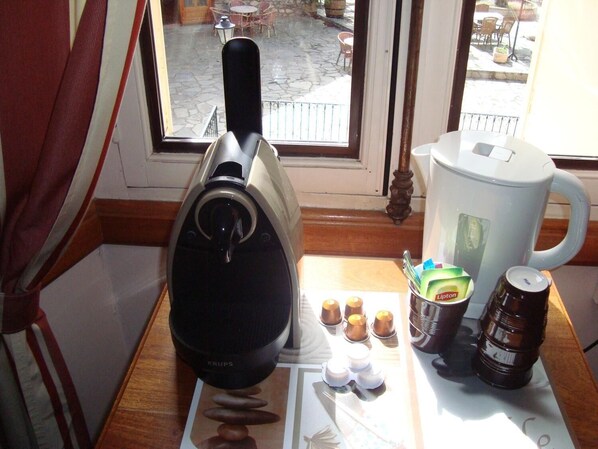 A coffee maker, a kettle, and a coffee cup on a table near a window.