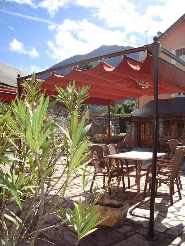 An outdoor patio with tables and chairs, surrounded by plants and a stone wall. - Grand Hôtel de France (Pierrefitte-Nestalas)