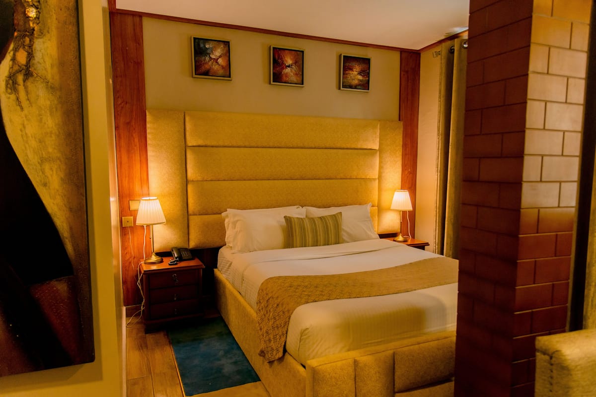 A hotel room with a large bed, two bedside lamps, a wooden headboard, and three paintings on the wall.