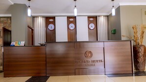 A reception desk with clocks displaying different time zones, a wooden finish, and a sign reading "LEGEND HOTEL KIGALI". - Legend Hotel (Kigali)