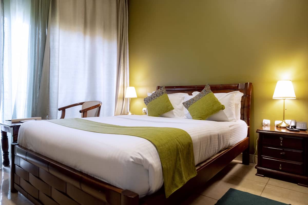 A neatly made bed with a green throw, two bedside lamps, and a wooden nightstand with a phone and a lamp.