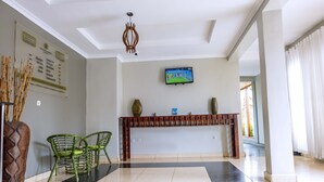 A hotel lobby with a reception desk, green chairs, a large vase, and a television displaying a tennis match. - Legend Hotel (Kigali)