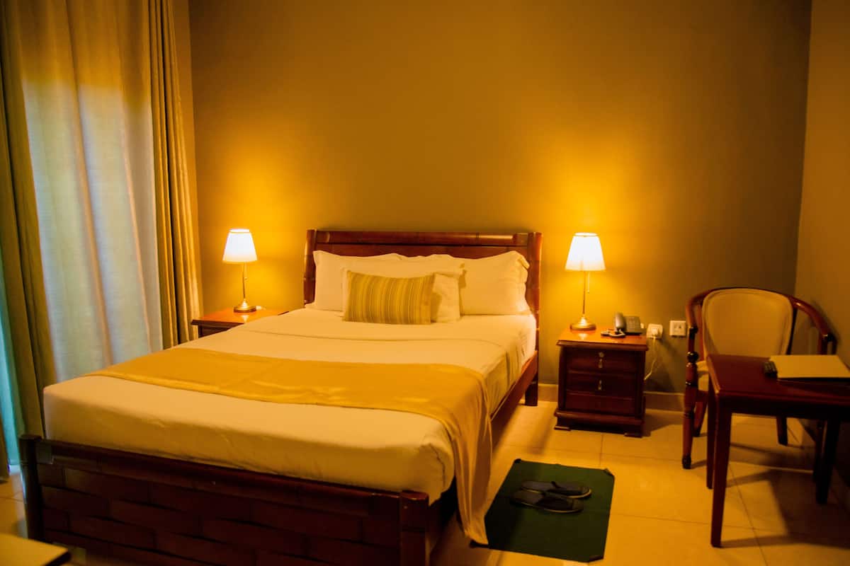 A hotel room with a large bed, two bedside lamps, a wooden nightstand, a chair, and a desk.