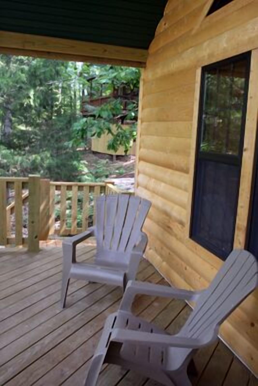 Een houten chalet met twee witte kunststof Adirondack stoelen op een houten terras.