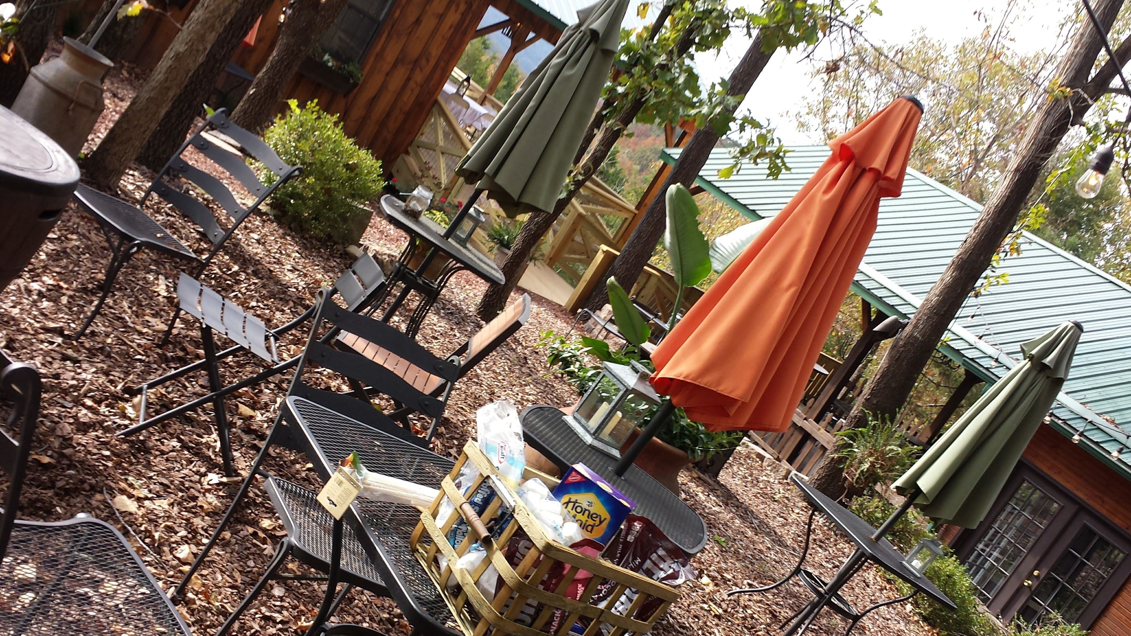 A patio area with metal chairs, a table with a basket of items, and a green umbrella.