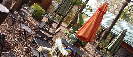 A patio area with metal chairs, a table with a basket of items, and a green umbrella.
