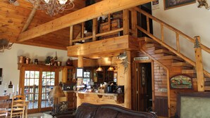 A rustic cabin interior with a wooden staircase, a dining area, and a kitchen. - Bear Creek Lodge Cabin Resort (Walnut Shade)