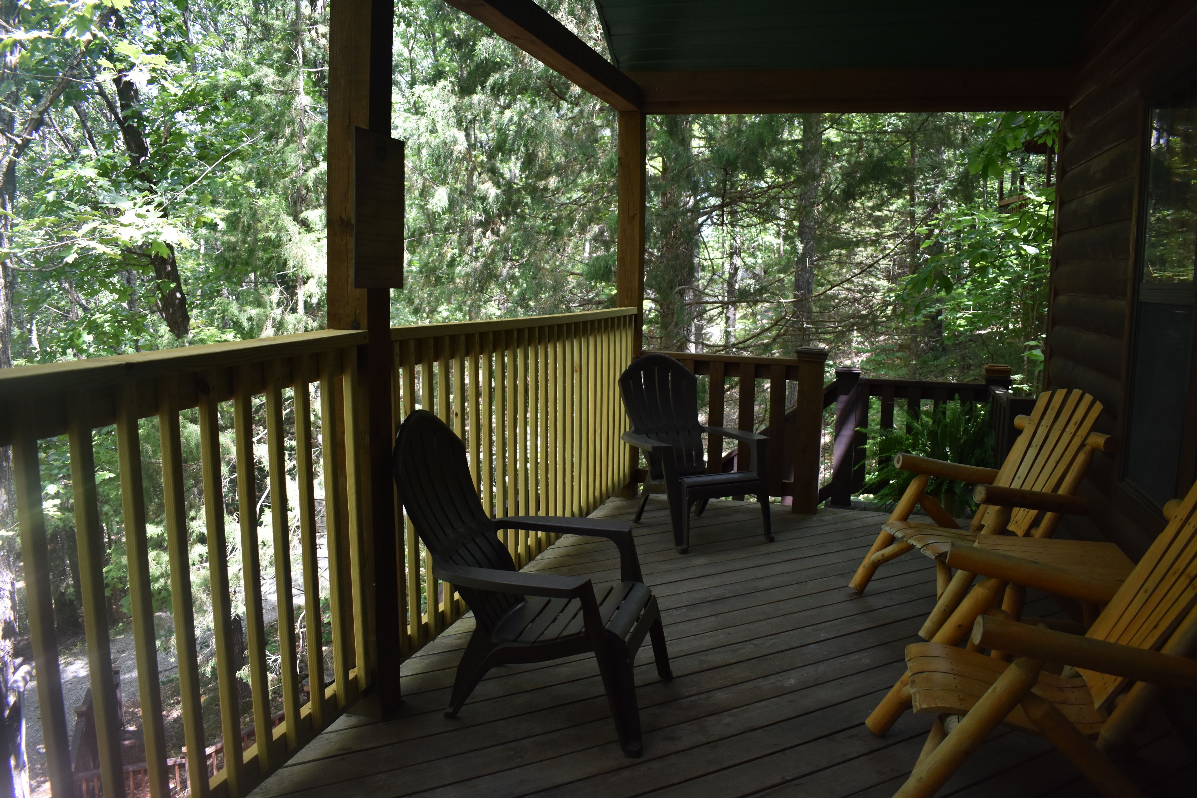 Un patio in legno con sedie e un tavolo, circondato da una fitta foresta.