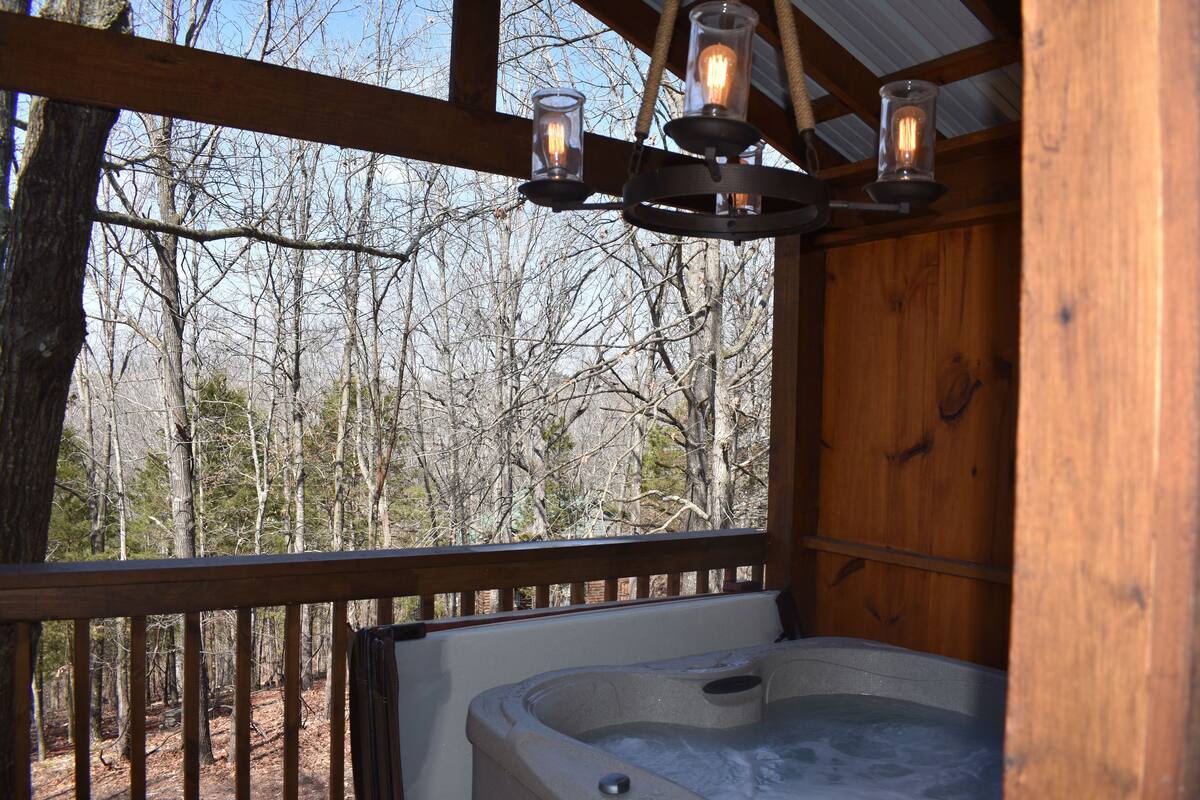 Een hottub met een houten terras en uitzicht op een bos.