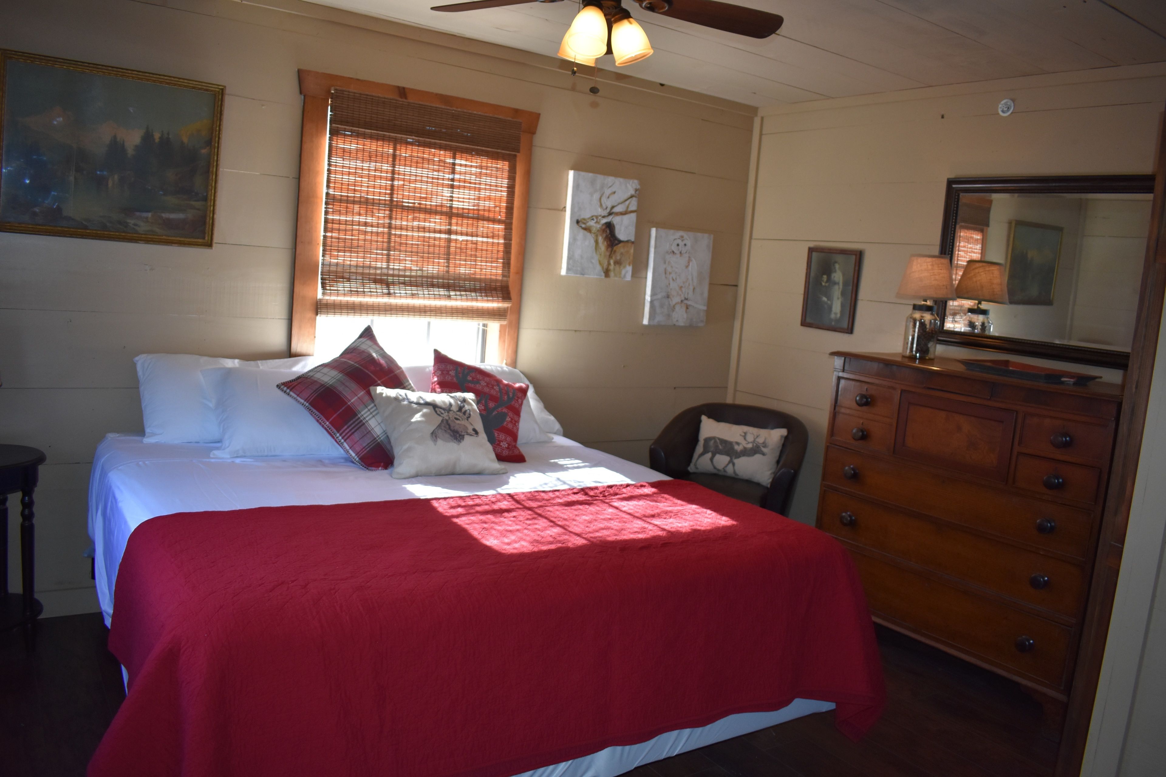 A bedroom with a bed, a dresser, a mirror, and a window with blinds.