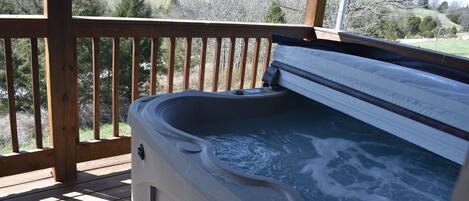 A hot tub on a wooden deck with a view of a grassy landscape.