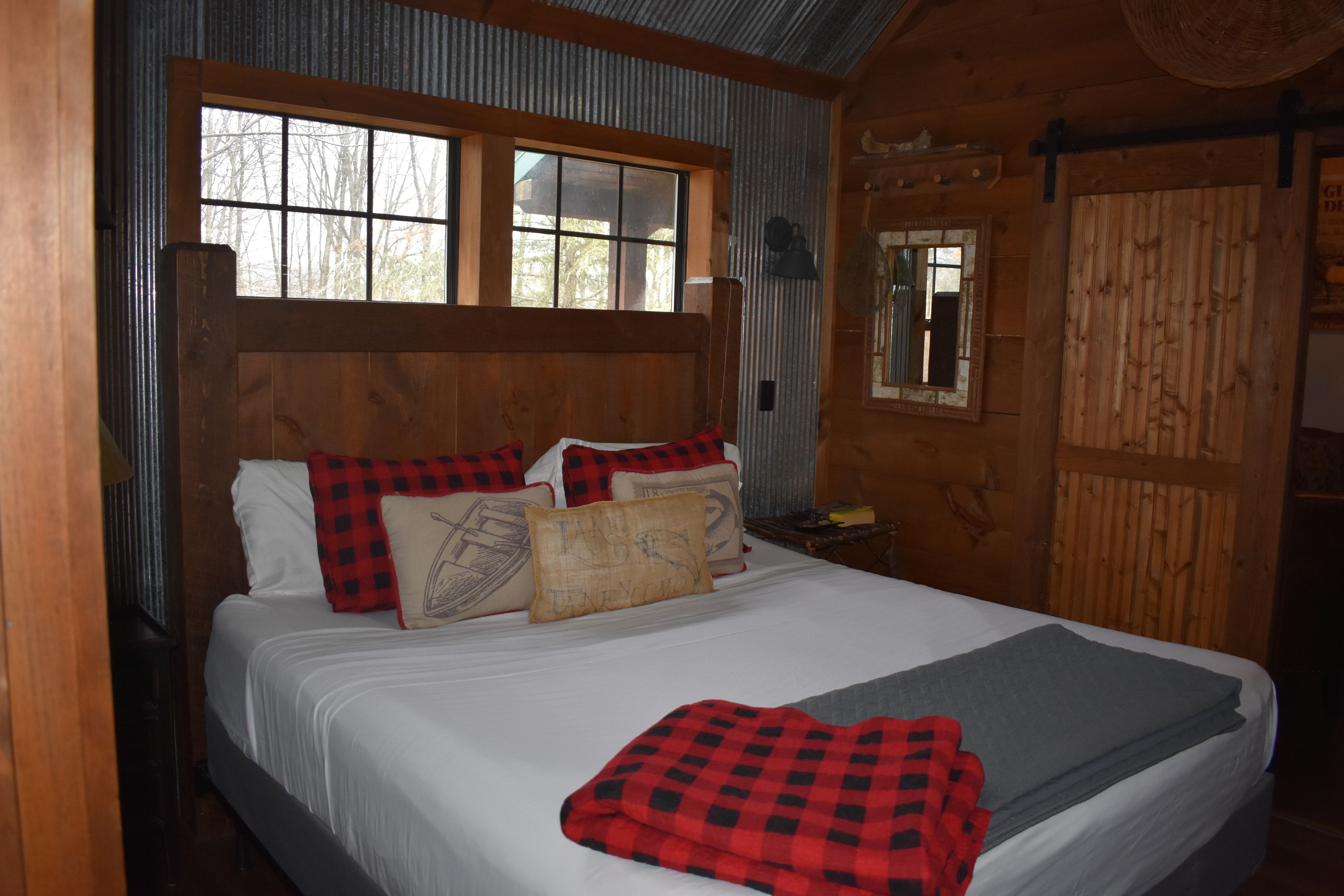 A wooden cabin bedroom with a large bed, a window, and a mirror on the wall.