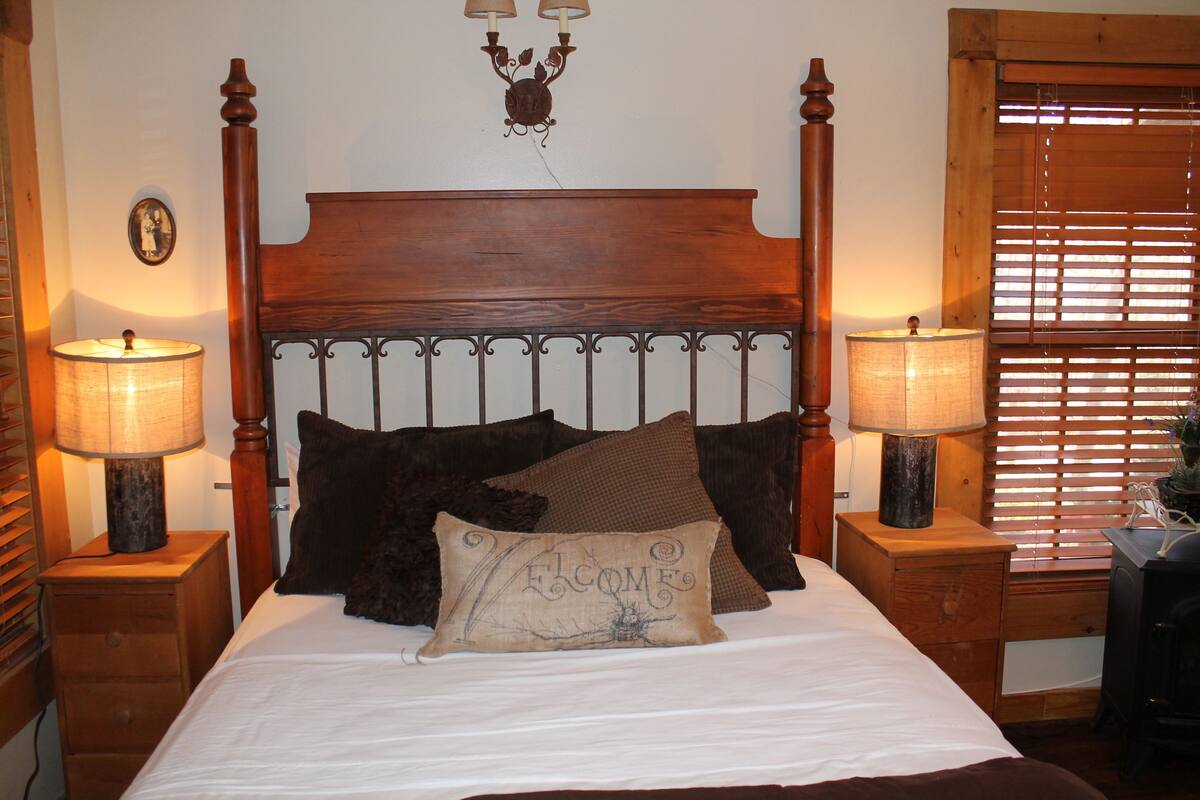 Een net opgemaakt bed met een houten hoofdeinde, twee bedlampjes en een welkomstkussen.