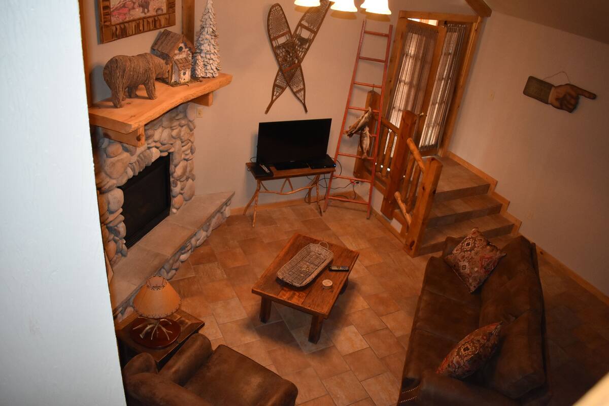 Een gezellige woonkamer met een open haard, een houten salontafel, een bank en een televisie op een standaard.