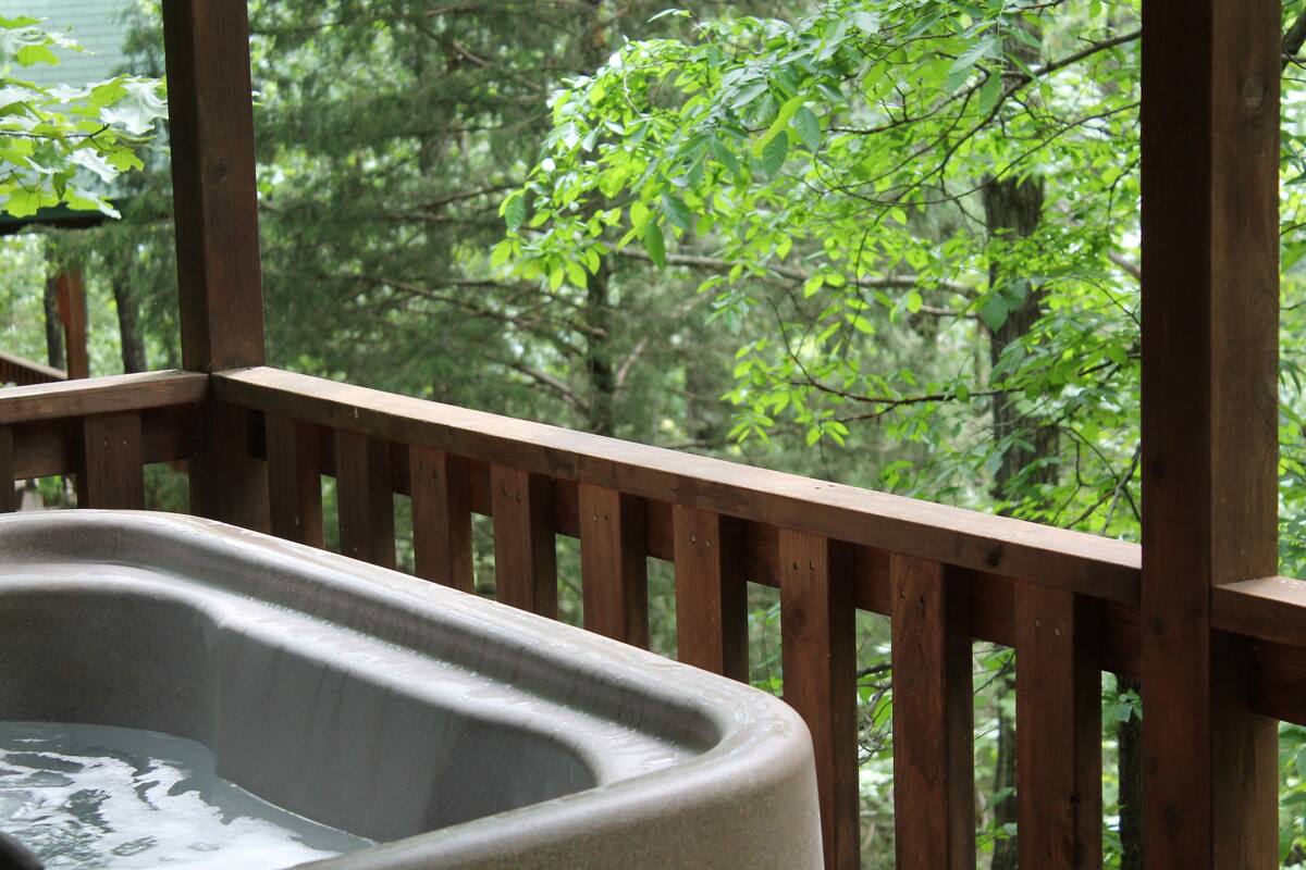 Een hottub op een houten terras met uitzicht op een bos.