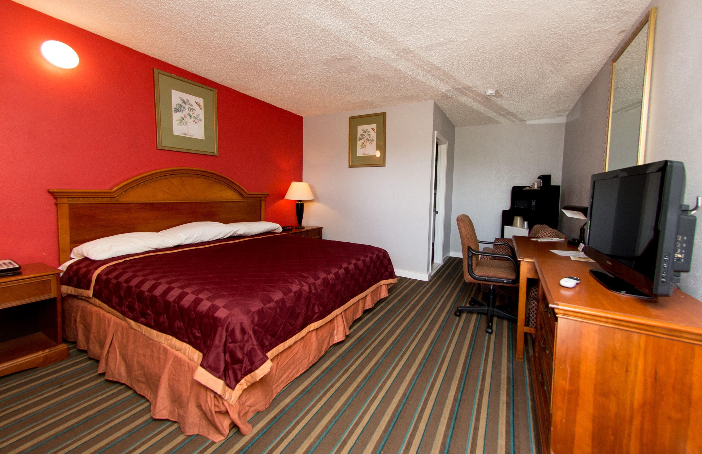 A hotel room with a large bed, a desk with a television, a chair, and a desk lamp.