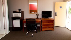 A hotel room with a wooden desk, a black office chair, a white refrigerator, a microwave, a television, and a door with a number sign. - Scottish Inn and Suites (Bensalem)