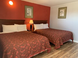 Habitación de hotel con dos camas, cada una con colcha estampada, una mesita de noche con lámpara y obras de arte botánicas enmarcadas en las paredes.