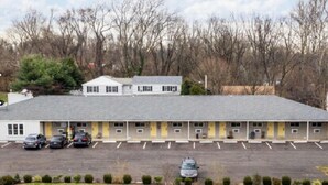 A motel with a flat roof, a parking lot, and a grassy area in front. - Scottish Inn and Suites (Bensalem)