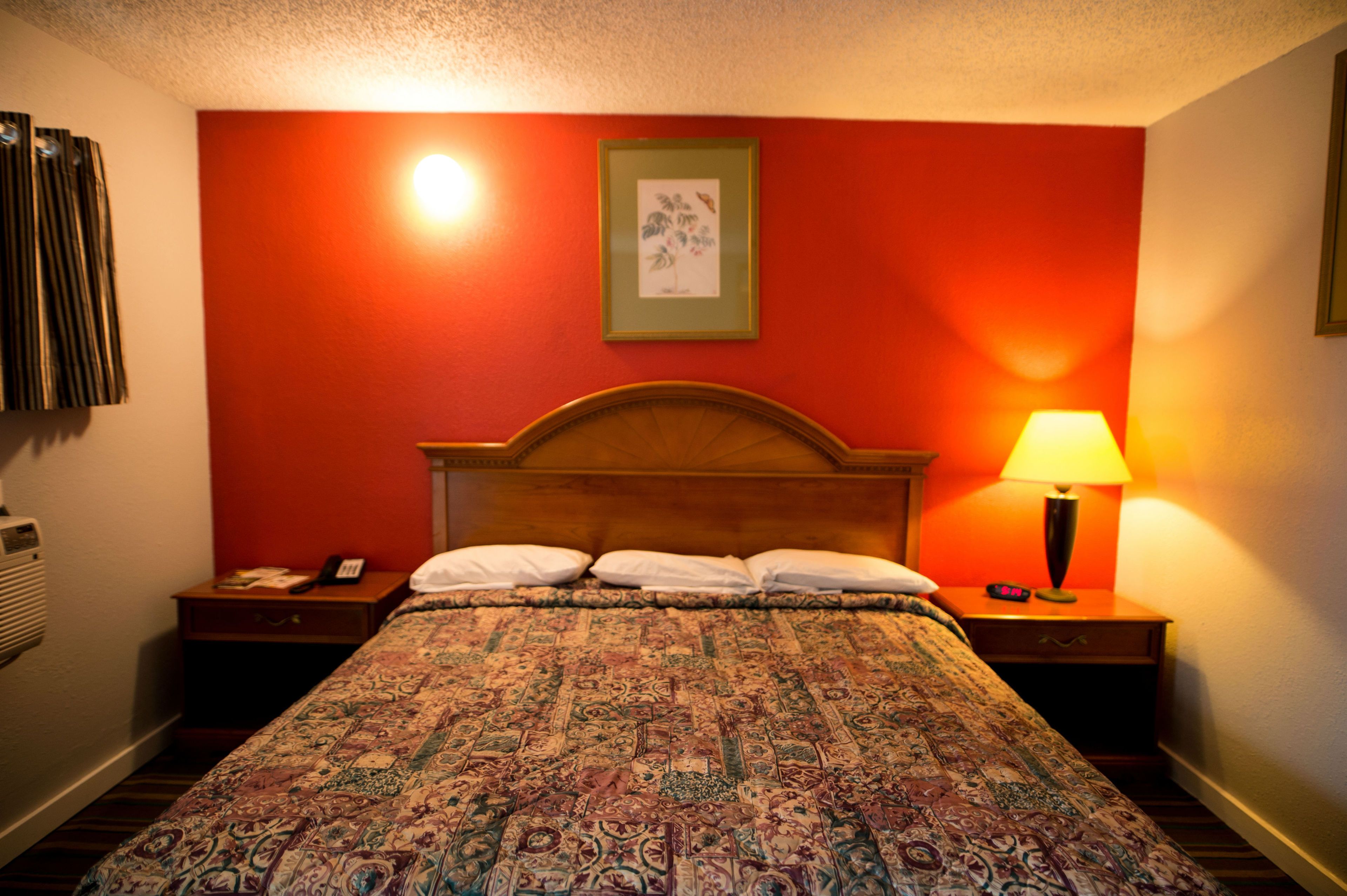 Una habitación de hotel con una cama grande, un cabecero de madera, una mesita de noche con una lámpara, un cuadro enmarcado en la pared y un teléfono sobre la mesita.