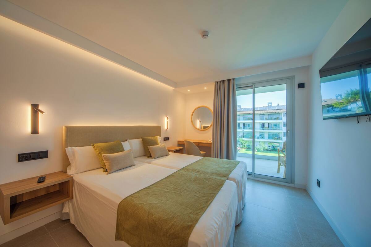 A modern hotel room with a large bed, a desk, a chair, a window, and a balcony.