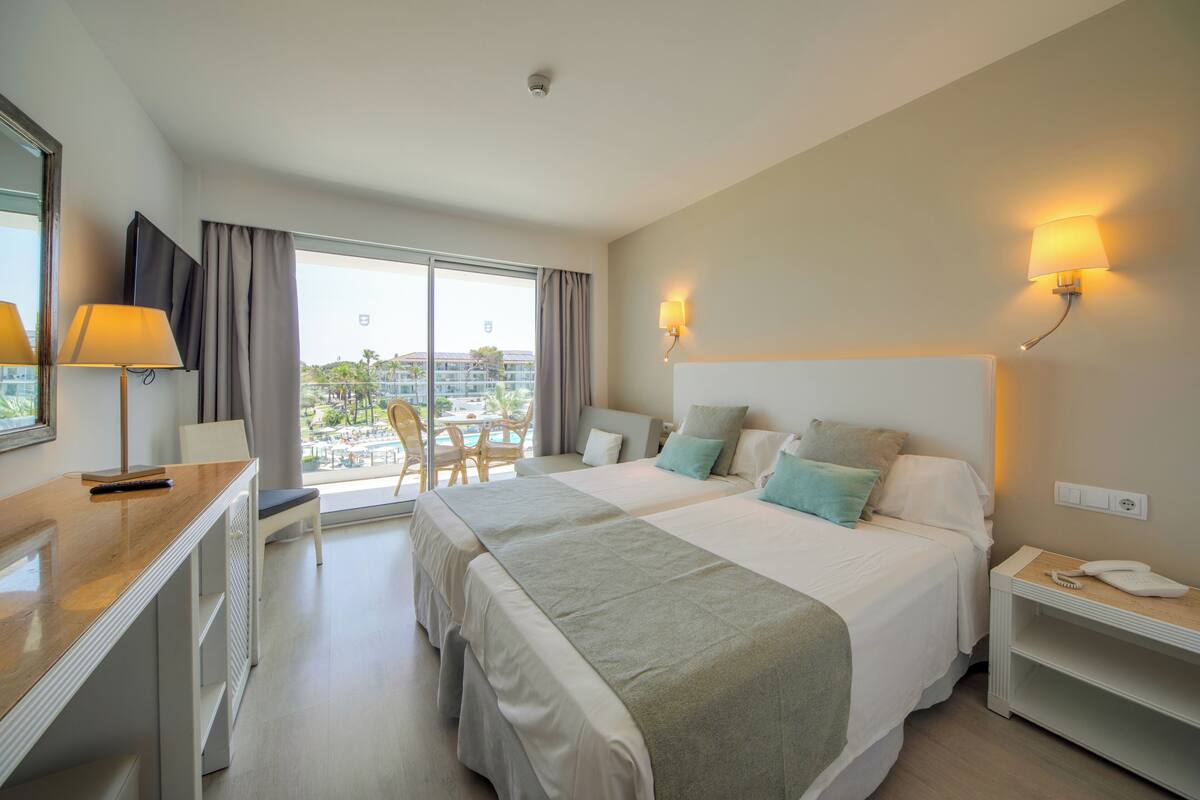 A hotel room with a large bed, a desk, a chair, and a view of the outdoors.