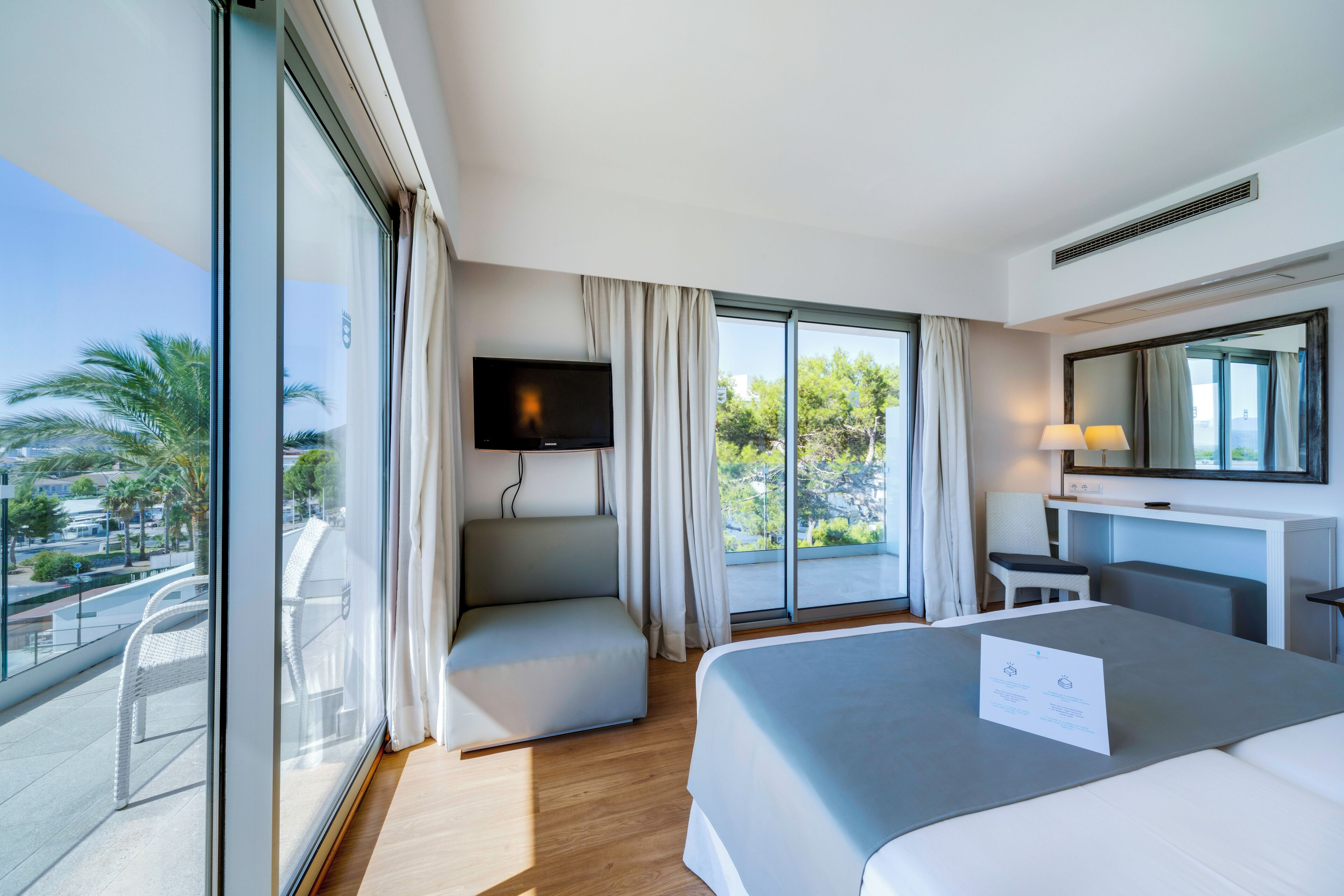 A modern hotel room with a large bed, a flat-screen TV, a desk, and a balcony with a view.