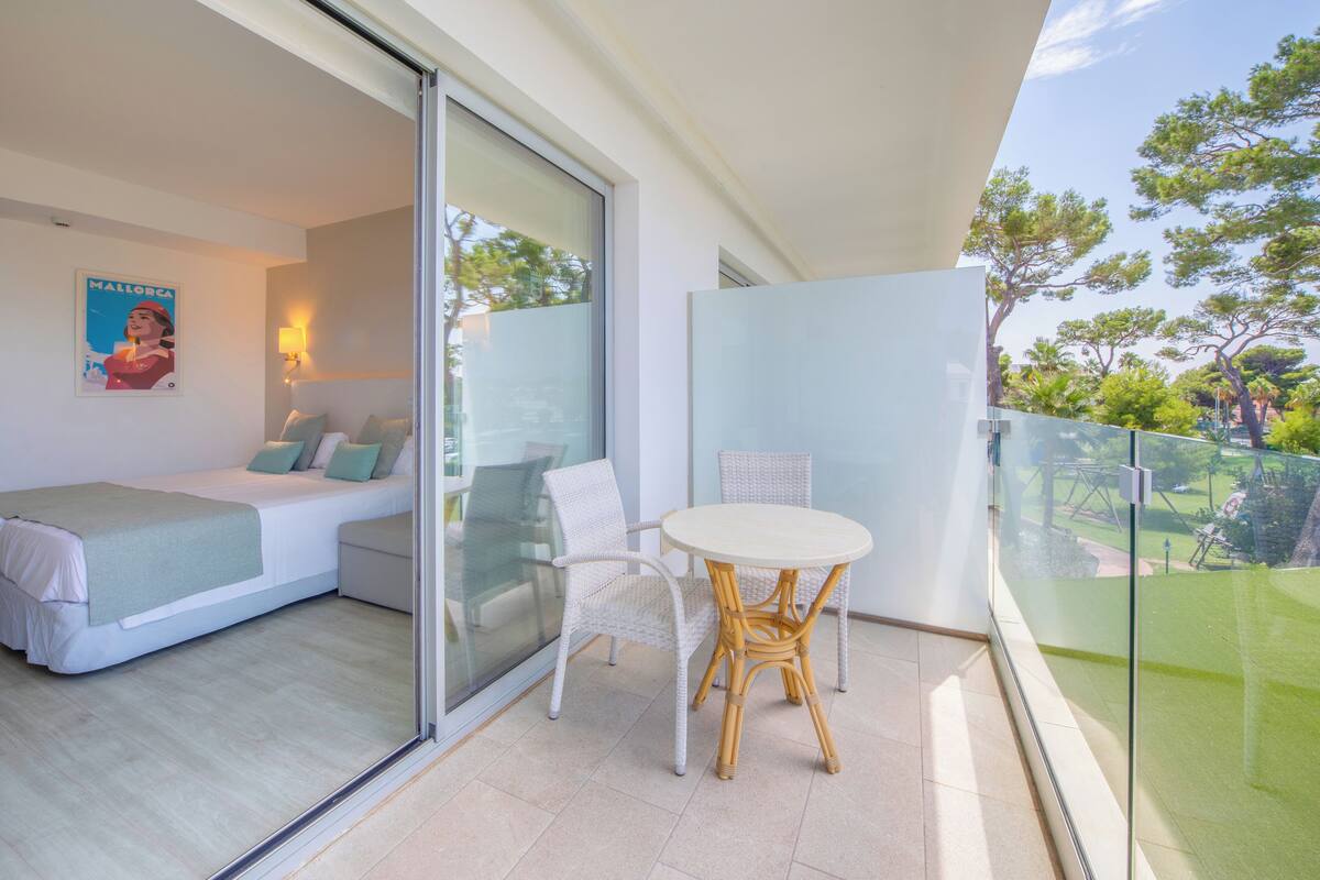 A balcony with a glass door leading to a bedroom, a wicker chair, and a small table.