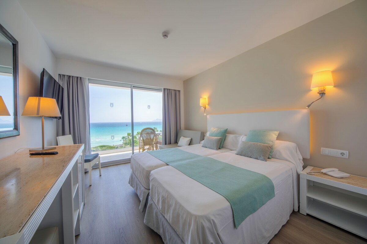A hotel room with a large bed, a desk, a chair, and a view of the ocean.
